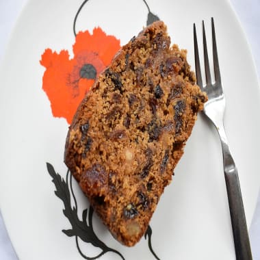 Slice of Old Fashioned Boiled Fruit Cake on a plate with a poppy pattern and a silver fork on the side.